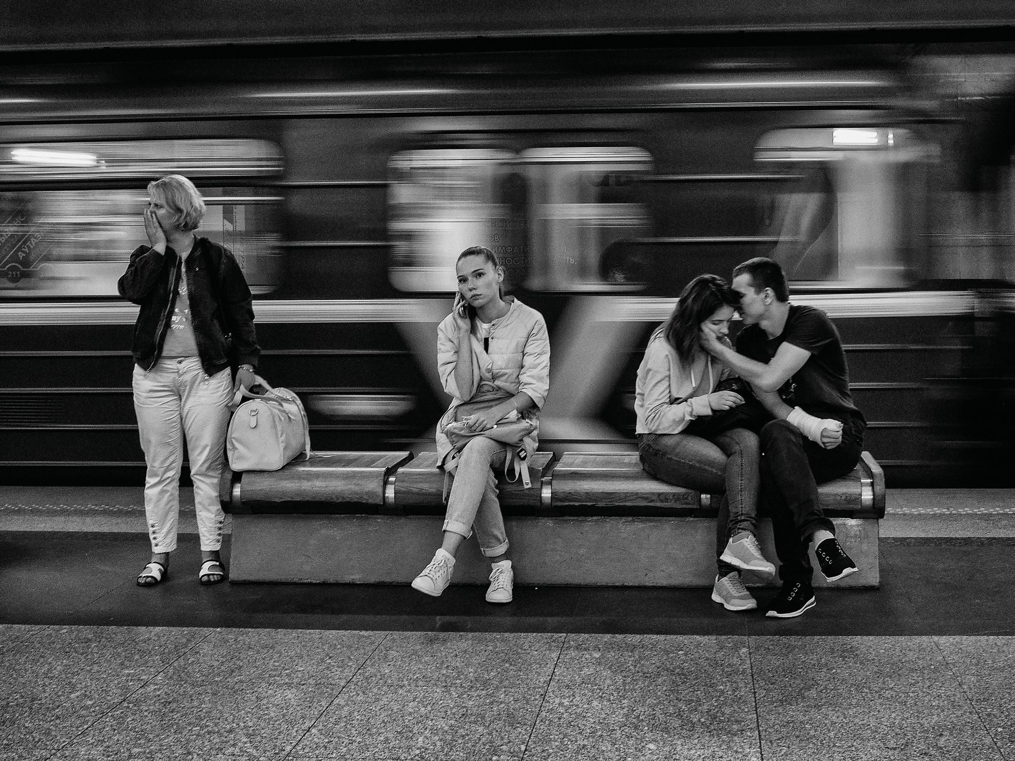 People waiting on a metro bench while a train blurs past behind them